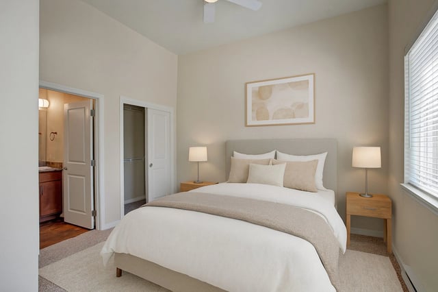 A bright bedroom with a queen-sized bed, nightstands, closet, and a door leading to a bathroom.