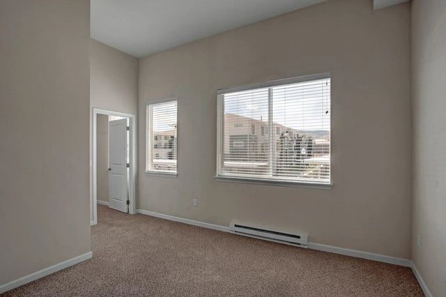 Empty bedroom with beige walls, beige carpet, and two windows with blinds.