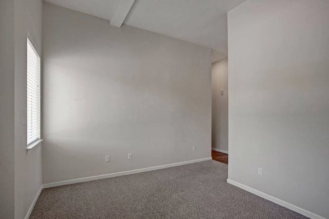 Empty room with neutral walls, carpet, and a window with blinds.