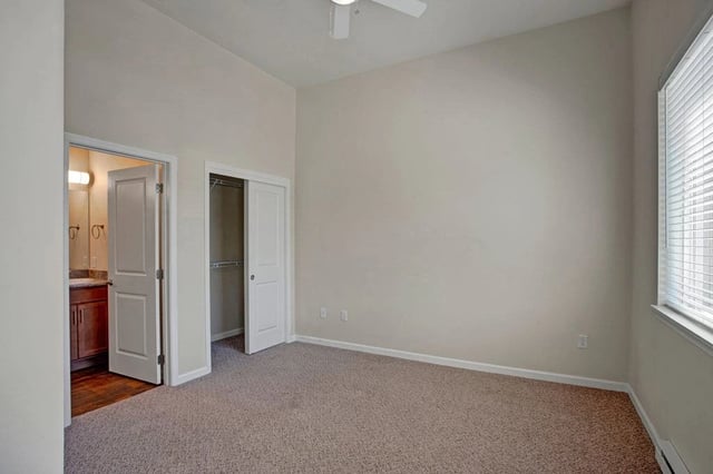 Bedroom with beige carpet, closet, and view into bathroom.