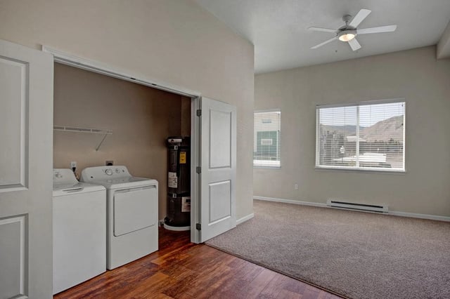 In-unit washer and dryer with water heater visible behind bi-fold doors, and view of a bedroom with a ceiling fan.