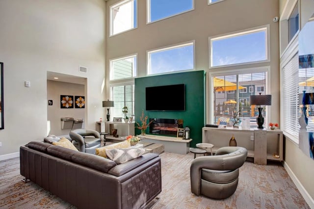Lounge area with a large sofa, chairs, fireplace, and TV, with windows overlooking the pool area.
