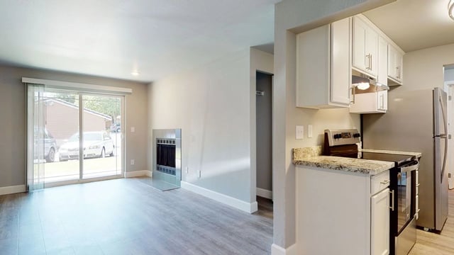 Living room with a fireplace and a view of the exterior through sliding glass doors, adjacent to a kitchen area.