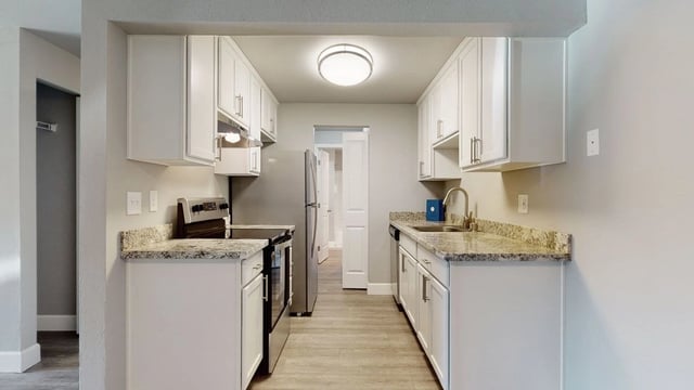 Modern galley kitchen with white cabinets, granite countertops, stainless steel appliances, and wood-look flooring.