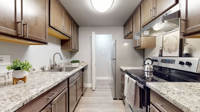 A galley kitchen with dark wood cabinets, granite countertops, and stainless steel appliances.