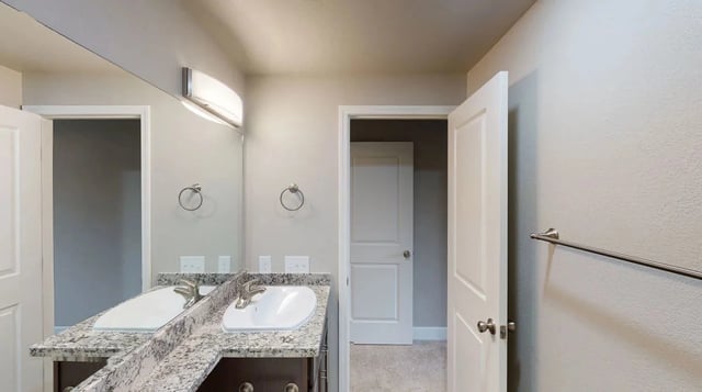 Bathroom vanity with dual sinks, granite countertops, and modern lighting.