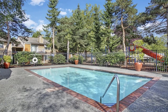 Outdoor swimming pool with a red slide and playground in the background.
