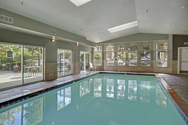 Indoor swimming pool area with lounge chairs and large windows.
