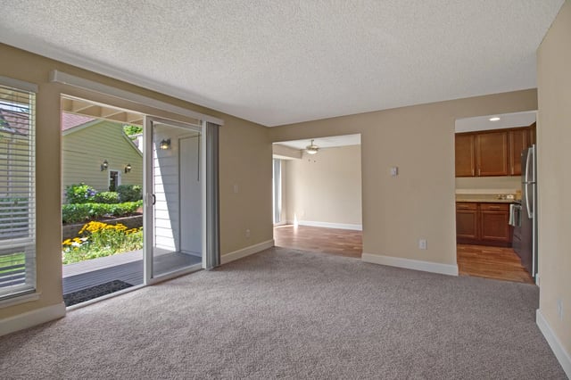 Living room with sliding glass door to a patio and view of garden, and opening to kitchen.