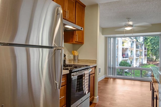 Stainless steel refrigerator and gas stove in a kitchen with wooden cabinets and a view of the apartment complex.