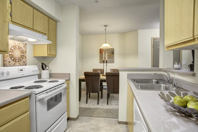 Kitchen with white appliances, light wood cabinets, and a view of the dining area.