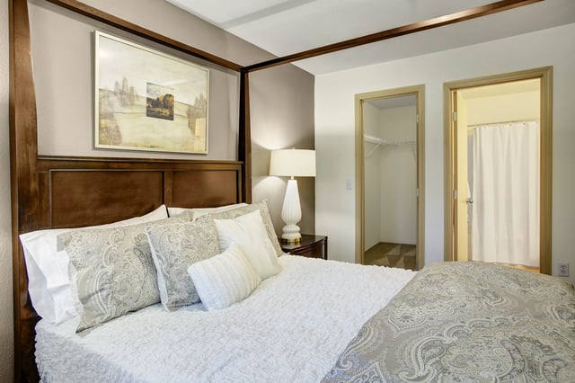 Bedroom with a large bed, decorative pillows, a nightstand with a lamp, and a view of a closet and bathroom.