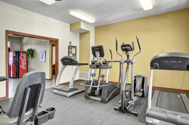 Fitness center with treadmills and elliptical machines. A Coca-Cola vending machine is visible in the background.