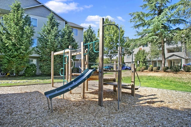 Playground with slide and monkey bars in front of apartment buildings.