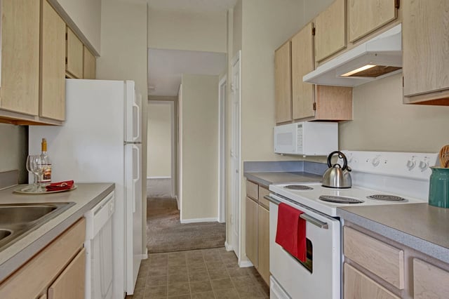 Kitchen with white appliances, light wood cabinets, and a hallway view.
