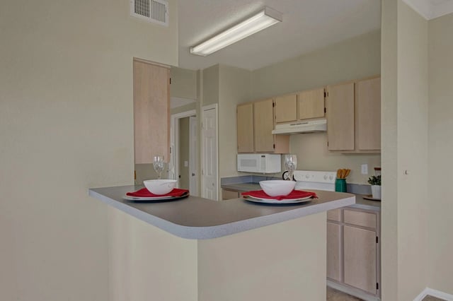 Kitchen with a breakfast bar featuring two place settings, cabinetry, and appliances.