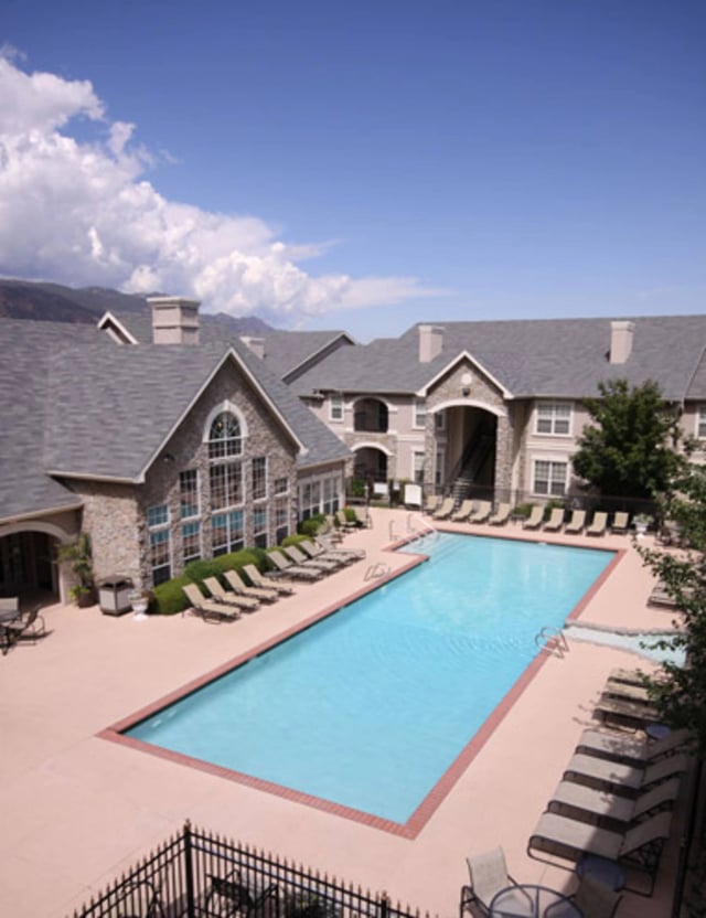 Outdoor swimming pool with lounge chairs and apartment buildings in the background.