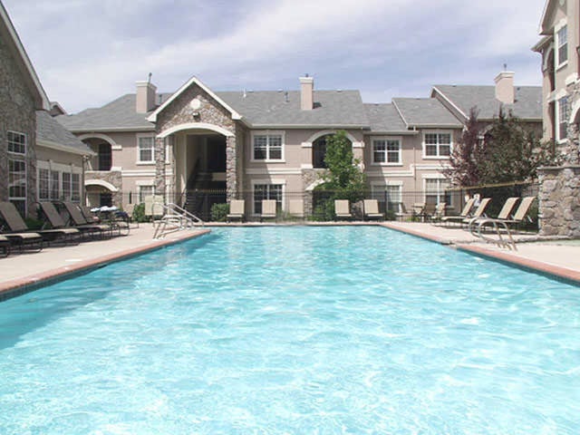 Outdoor swimming pool and lounge chairs with apartment buildings in the background.
