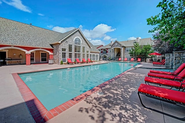 Luxury apartment complex swimming pool with red lounge chairs and a clear blue sky.