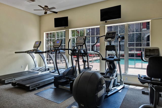 Fitness center with treadmills, elliptical machines, and a recumbent bike, overlooking the pool.