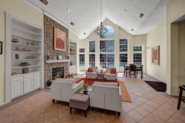 Spacious clubhouse with a stone fireplace, built-in bookshelves, and large windows overlooking the pool area.