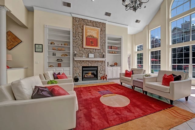 Spacious living area with a stone fireplace, white couches, and large windows overlooking a pool.