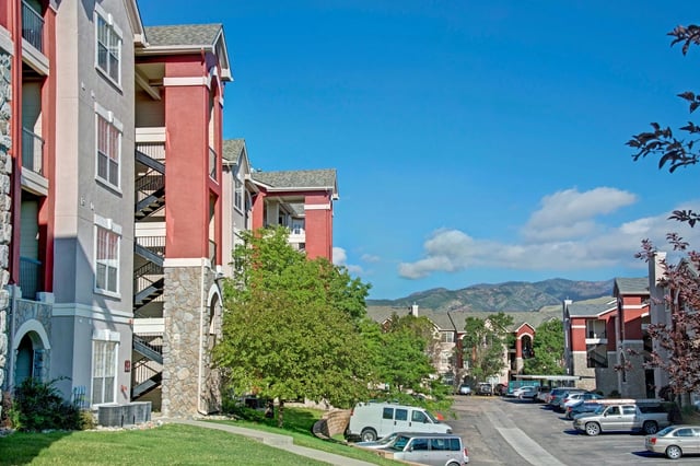 Apartment buildings with red and gray facades, exterior staircases, and a parking lot in front.