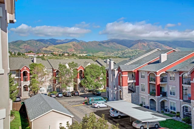 Apartment buildings with red accents and balconies, set against a backdrop of mountains and blue sky.