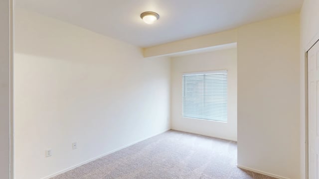 Empty bedroom with carpet, window with blinds, and light fixture.
