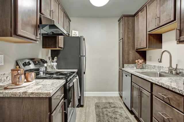 Modern kitchen with dark wood cabinets, granite countertops, stainless steel appliances, and a sink.
