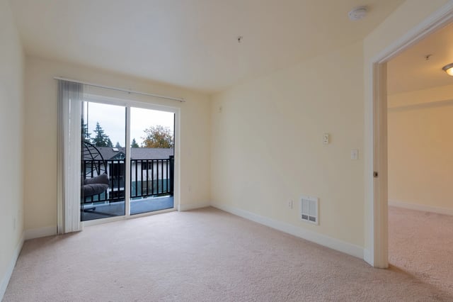 Interior view of a carpeted room with a sliding glass door leading to a balcony with a hanging chair.
