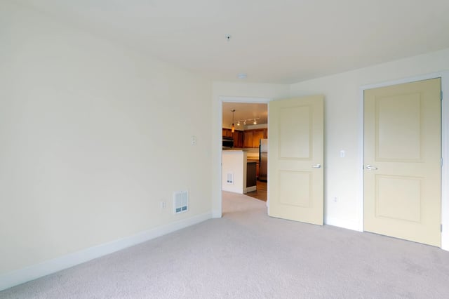 Interior view of a carpeted room with two closed doors and a view into a kitchen.