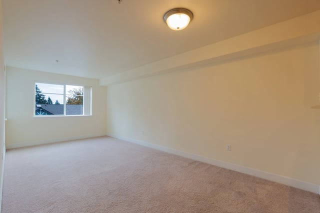 Empty living room with a large window and neutral carpet.