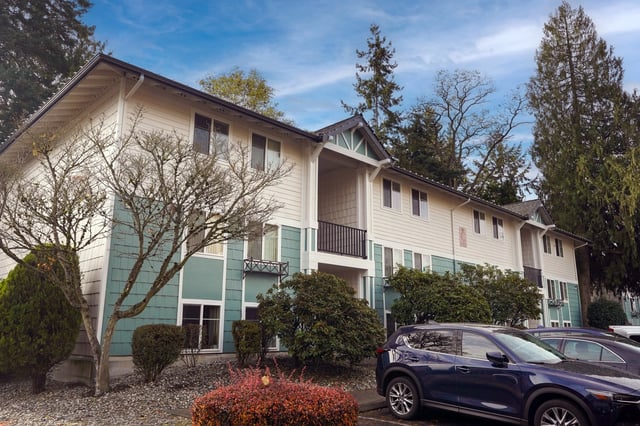 Exterior view of apartment building with teal and cream siding and trees.