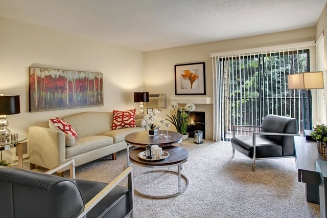 Living room with a fireplace, modern furniture, and large windows overlooking trees.