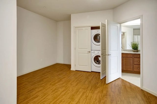 In-unit washer and dryer stack with closet doors open, adjacent to a bathroom.
