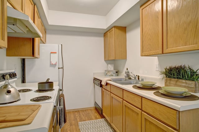 Kitchen with light wood cabinets, white countertops, stainless steel sink, dishwasher, and white stove.