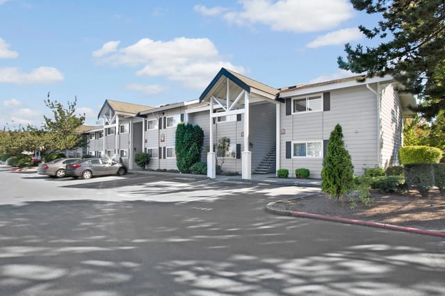 Apartment building exterior with parking lot and trees.