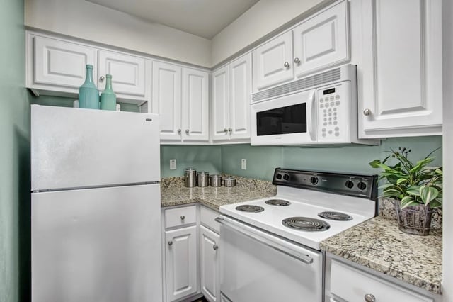 Modern white kitchen with granite countertops, stainless steel appliances, and pale green walls.