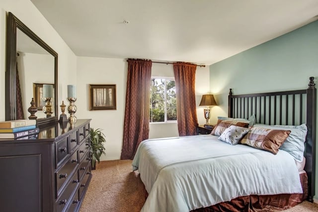 A furnished bedroom with a large bed, dresser, and mirror.