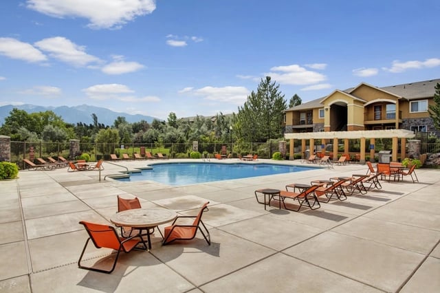 Outdoor swimming pool with lounge chairs and tables, mountain view.