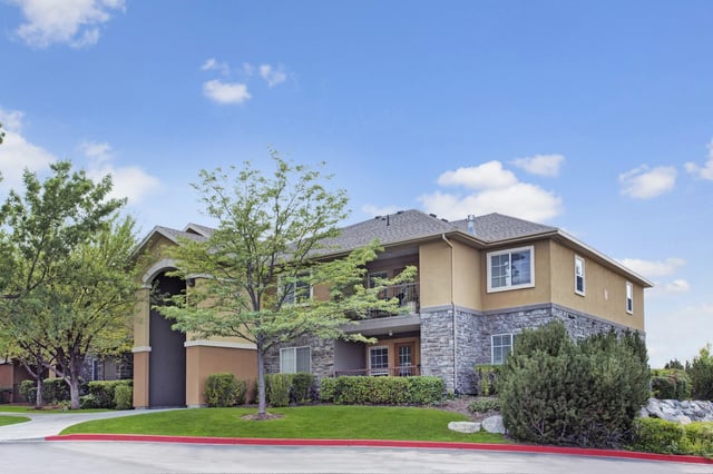 Exterior view of a multifamily apartment building with tan siding and stone accents under a blue sky.