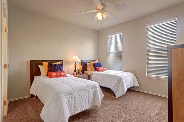 A bedroom with two twin beds, nightstand, and ceiling fan.
