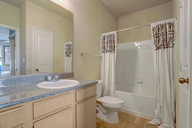 A clean bathroom with a granite countertop vanity, a white sink, a toilet, and a bathtub with a decorative shower curtain.