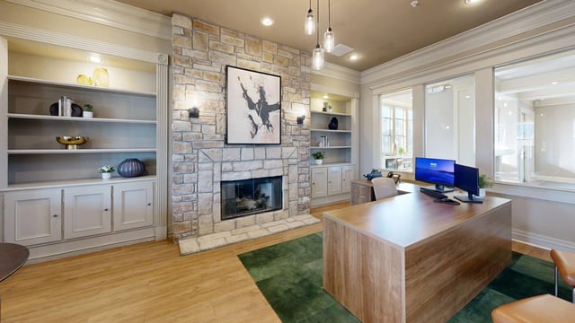 A modern office space with a stone fireplace, built-in bookshelves, and a large wooden desk.