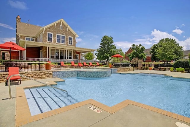 Outdoor swimming pool and hot tub area with lounge chairs and a clubhouse in the background.
