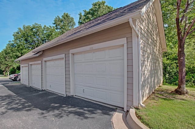 Row of white garage doors on a beige building exterior with trees and blue sky in background.