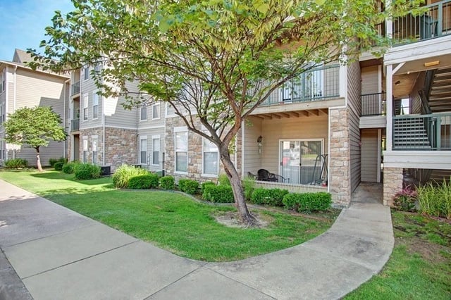 Exterior view of apartment building with balconies, green lawn, and walkway.