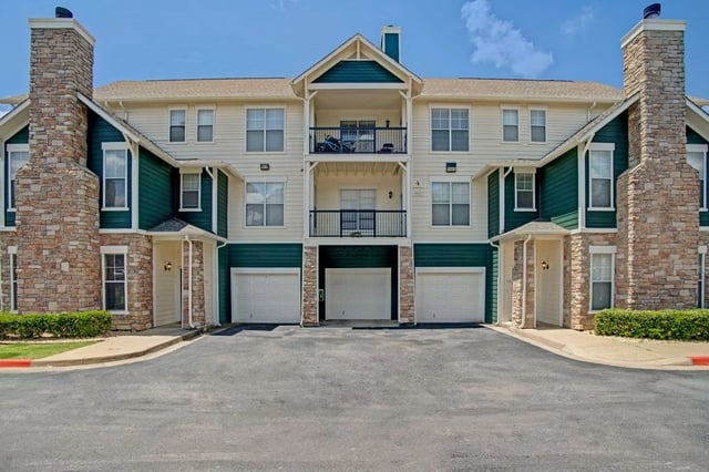 Exterior view of an apartment building with stone accents, green siding, and garages.