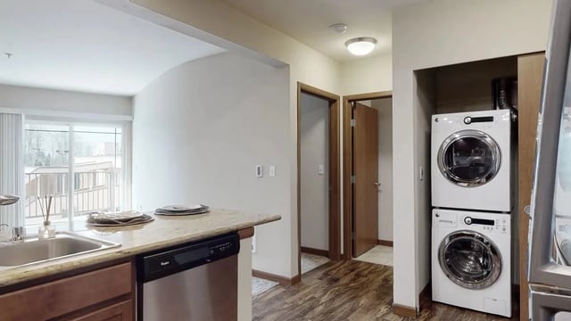 Kitchenette area with granite countertops, stainless steel sink, and dishwasher next to a stacked washer and dryer.